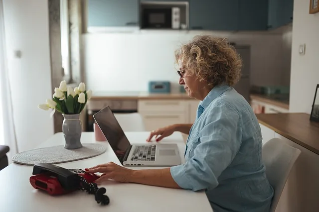 Woman over 50 working on a laptop at her kitchen table on a second income project