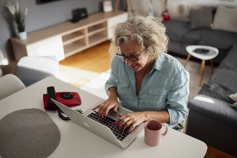 Smiling woman over 50 working on a laptop at home, building a second income